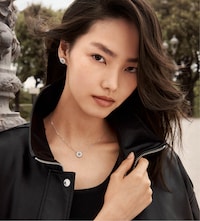 A person wearing a black jacket, adorned with Michael Kors sparkling silver necklace and stud earrings, poses outdoors with soft, flowing hair. image