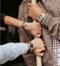 Three hands wearing stylish watches hold onto a pole, showcasing the unique designs of Sekonda watches against a casual backdrop. image