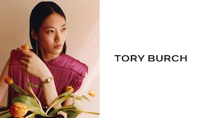 A lady in a vibrant pink top holds a bouquet of yellow tulips, next to the text "TORY BURCH" in bold black letters. image